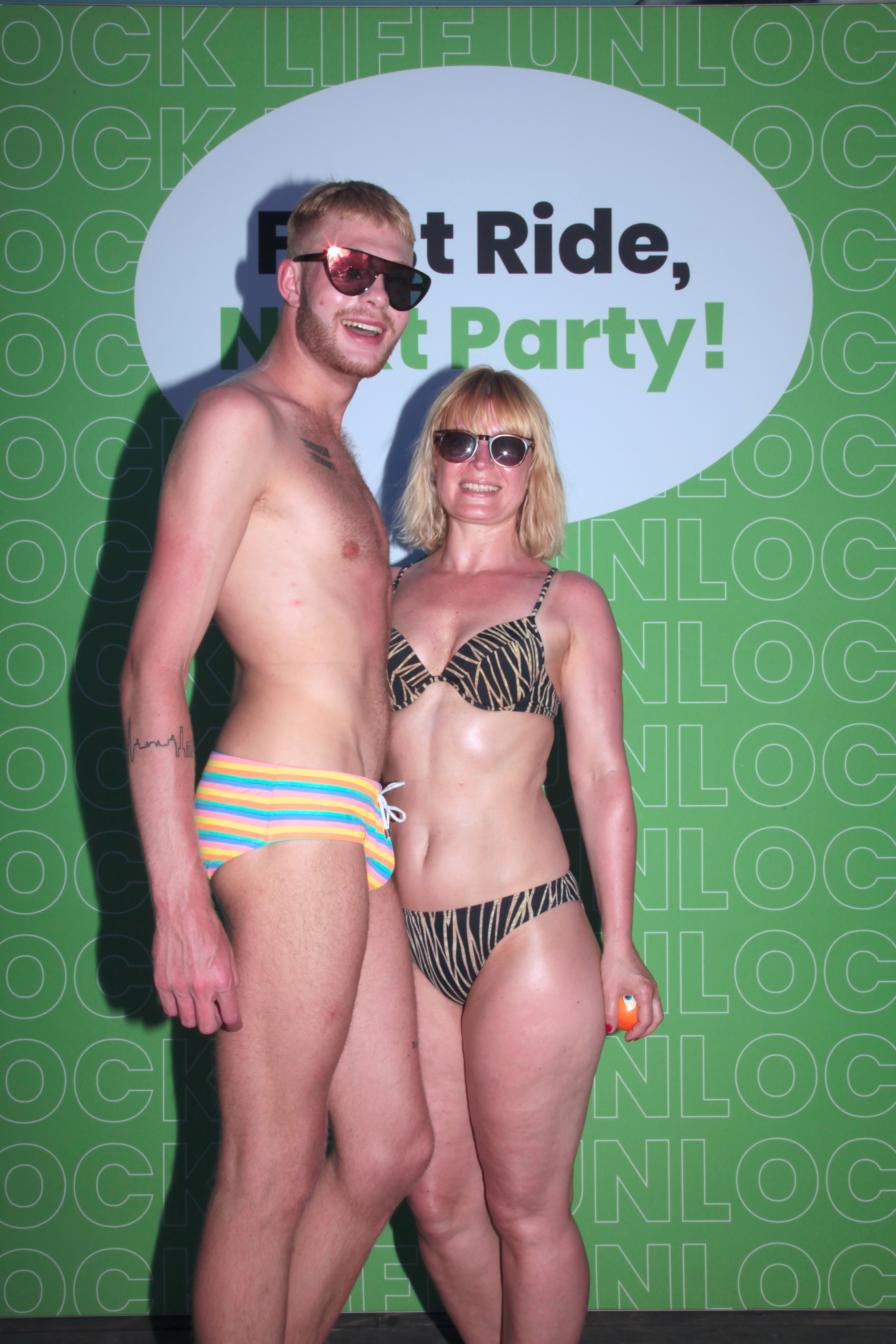 Two guests posing in front of a 'First Ride, Next Party!' photo backdrop