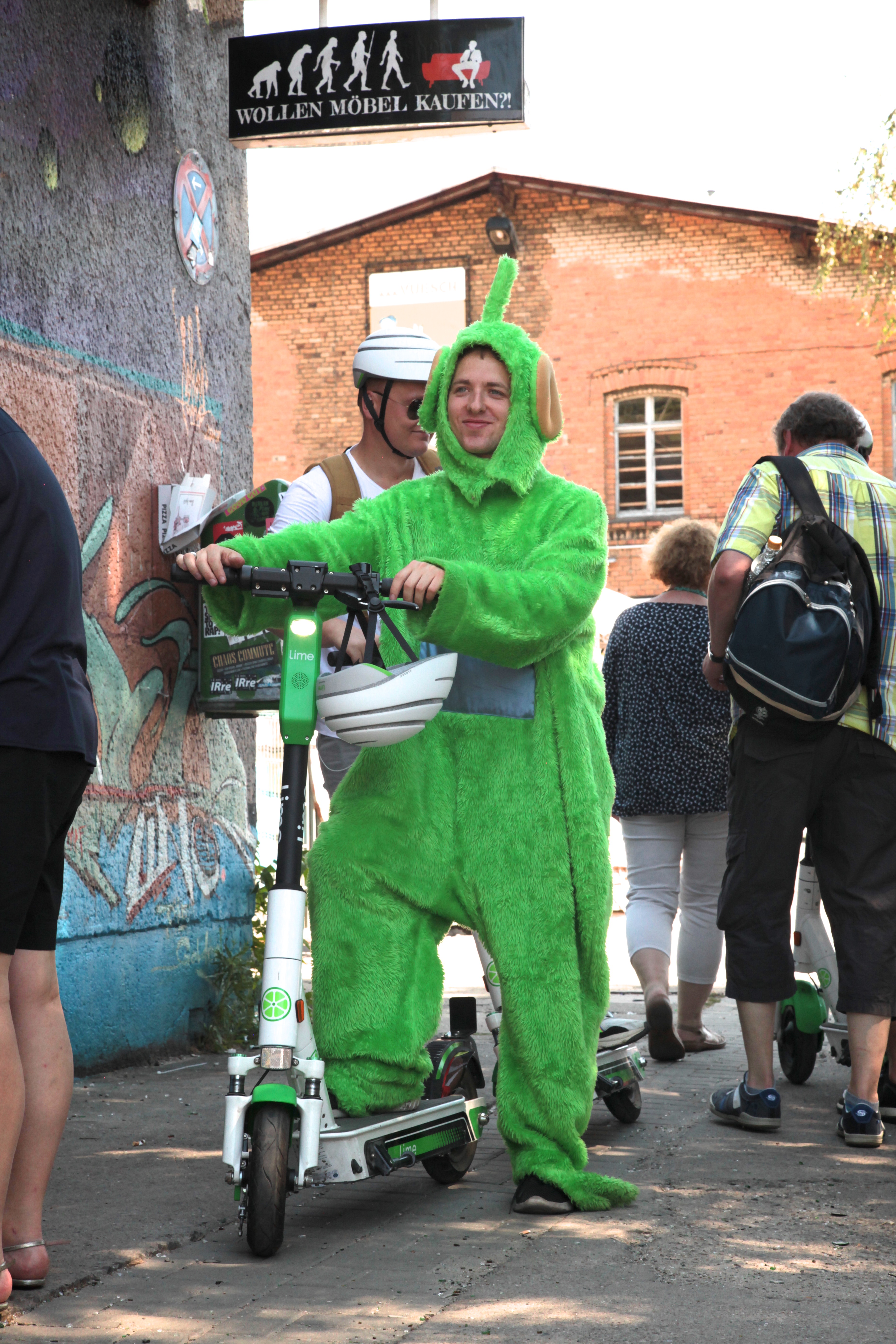 A guest in a green Lime mascot costume riding an e-scooter