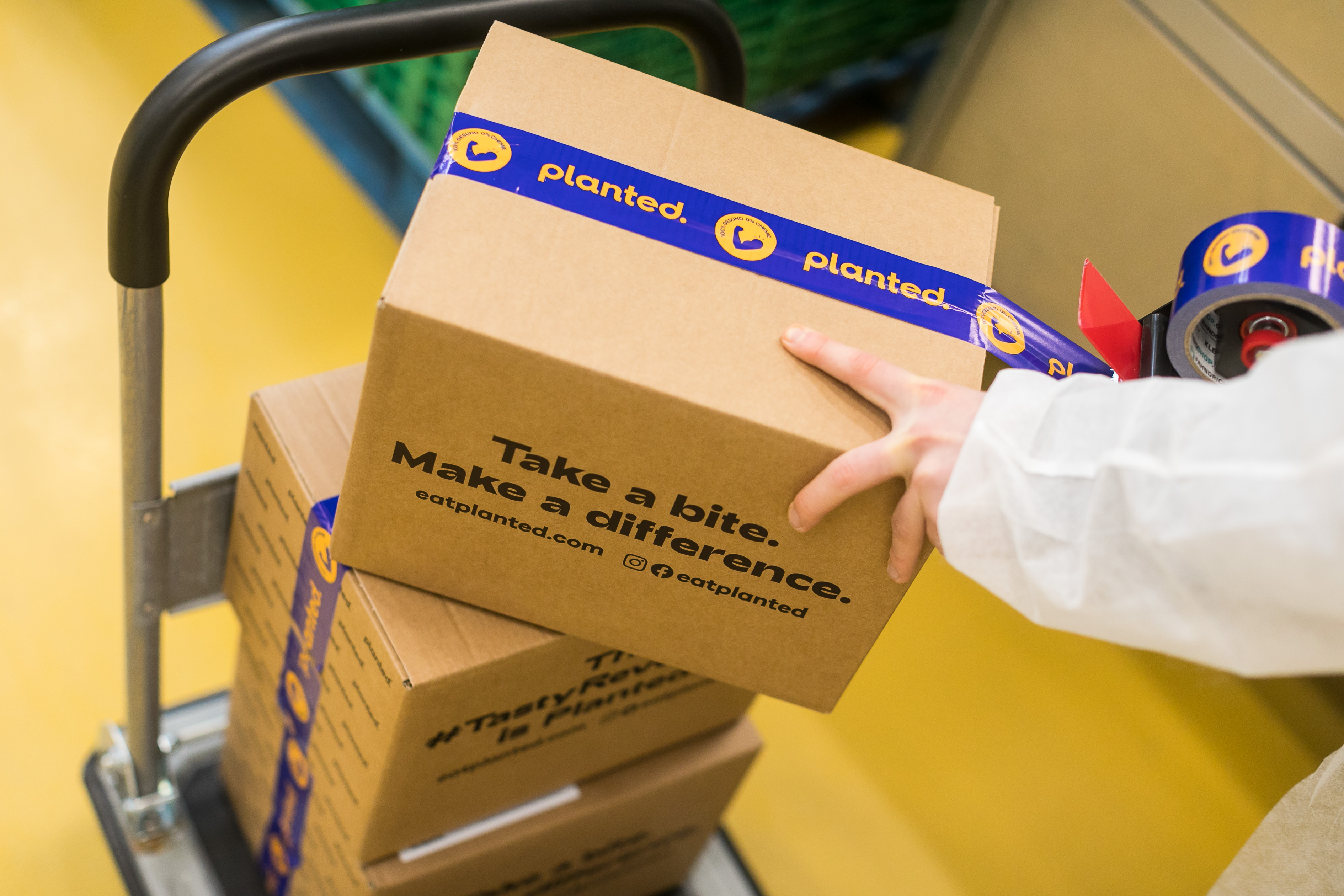 A hand taping a Planted delivery box reading 'Take a bite. Make a difference.'