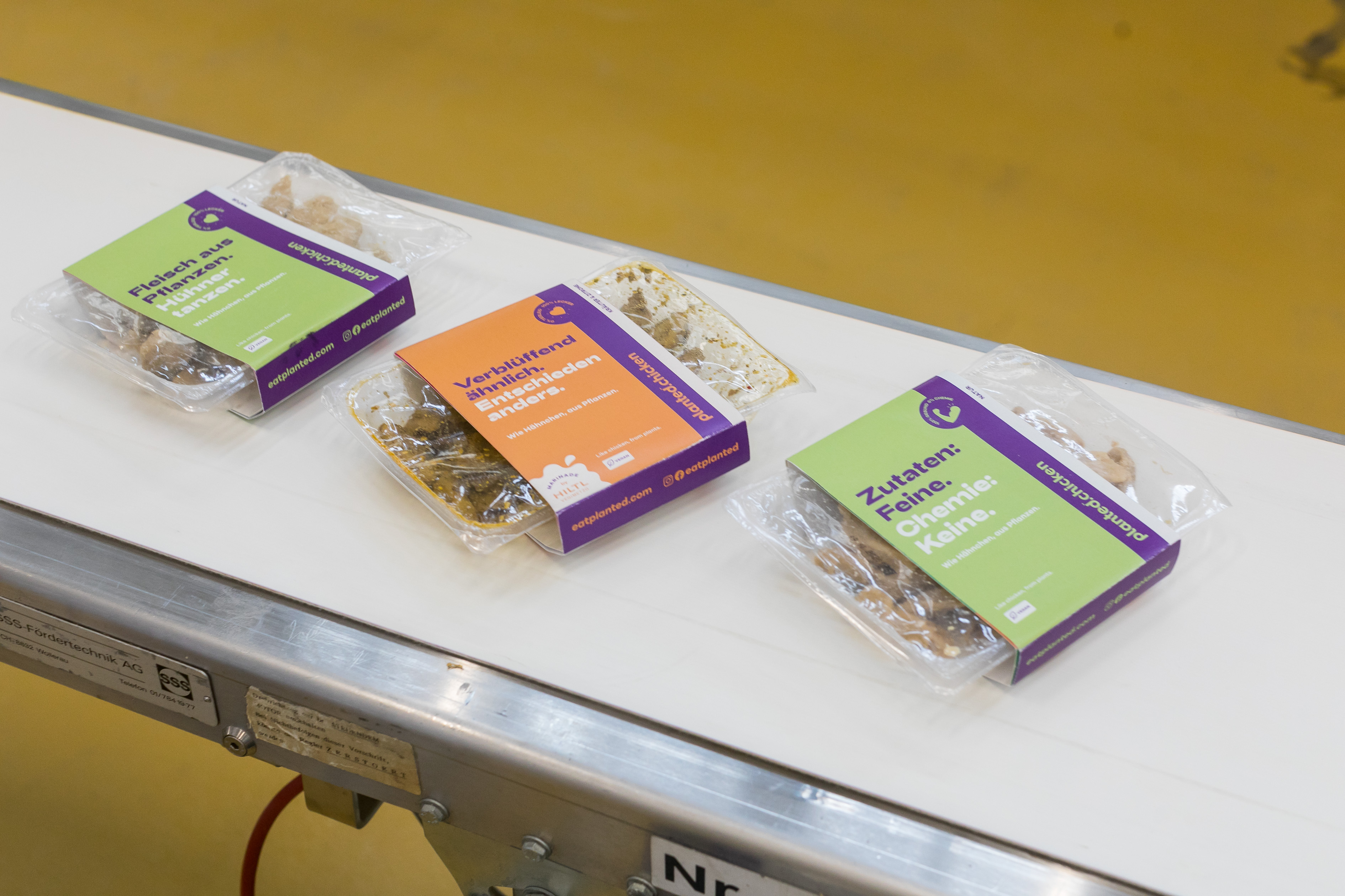 Three planted.chicken packs on a factory conveyor belt