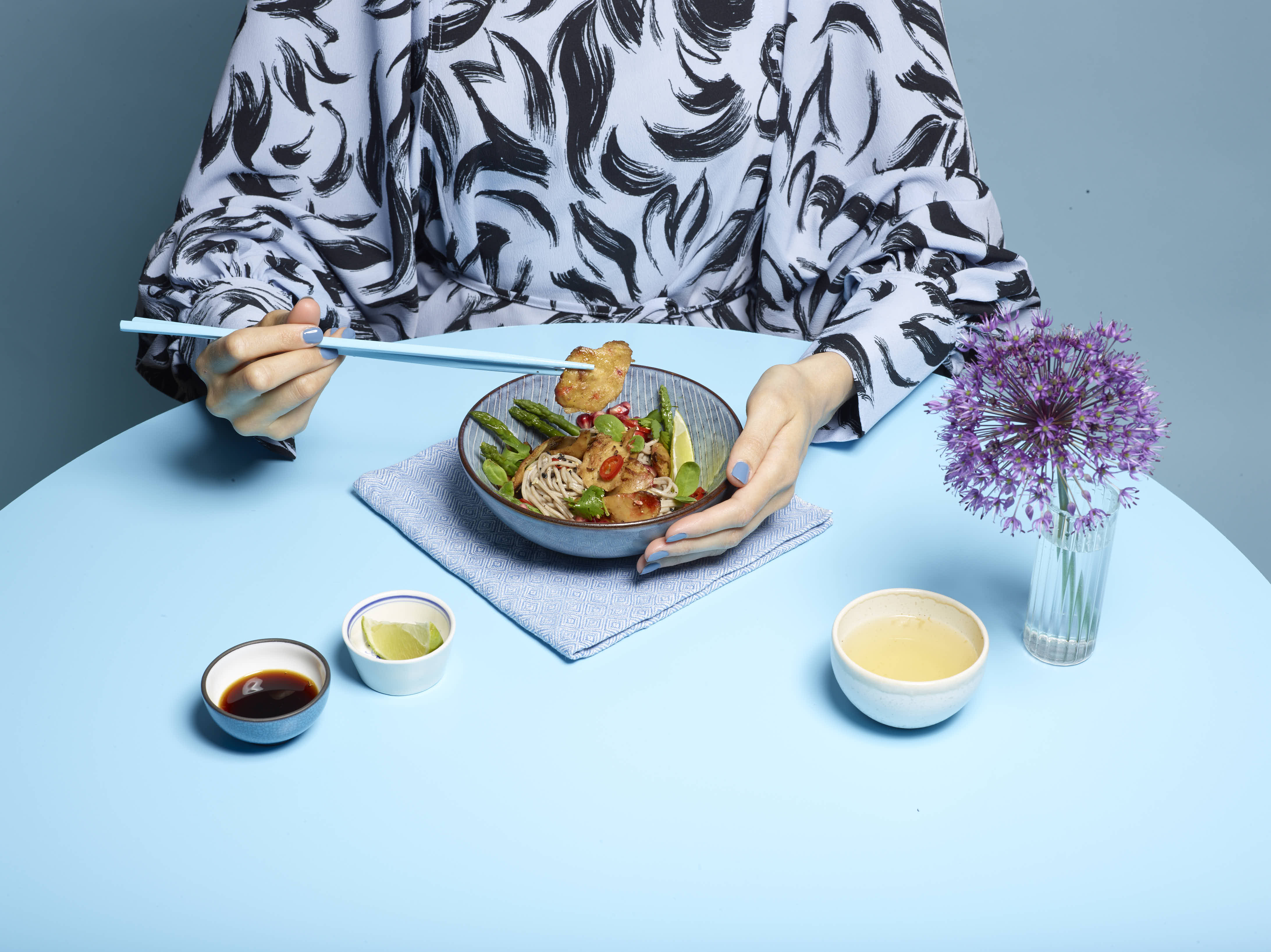 A bowl of planted.chicken noodles being eaten with chopsticks on a blue table