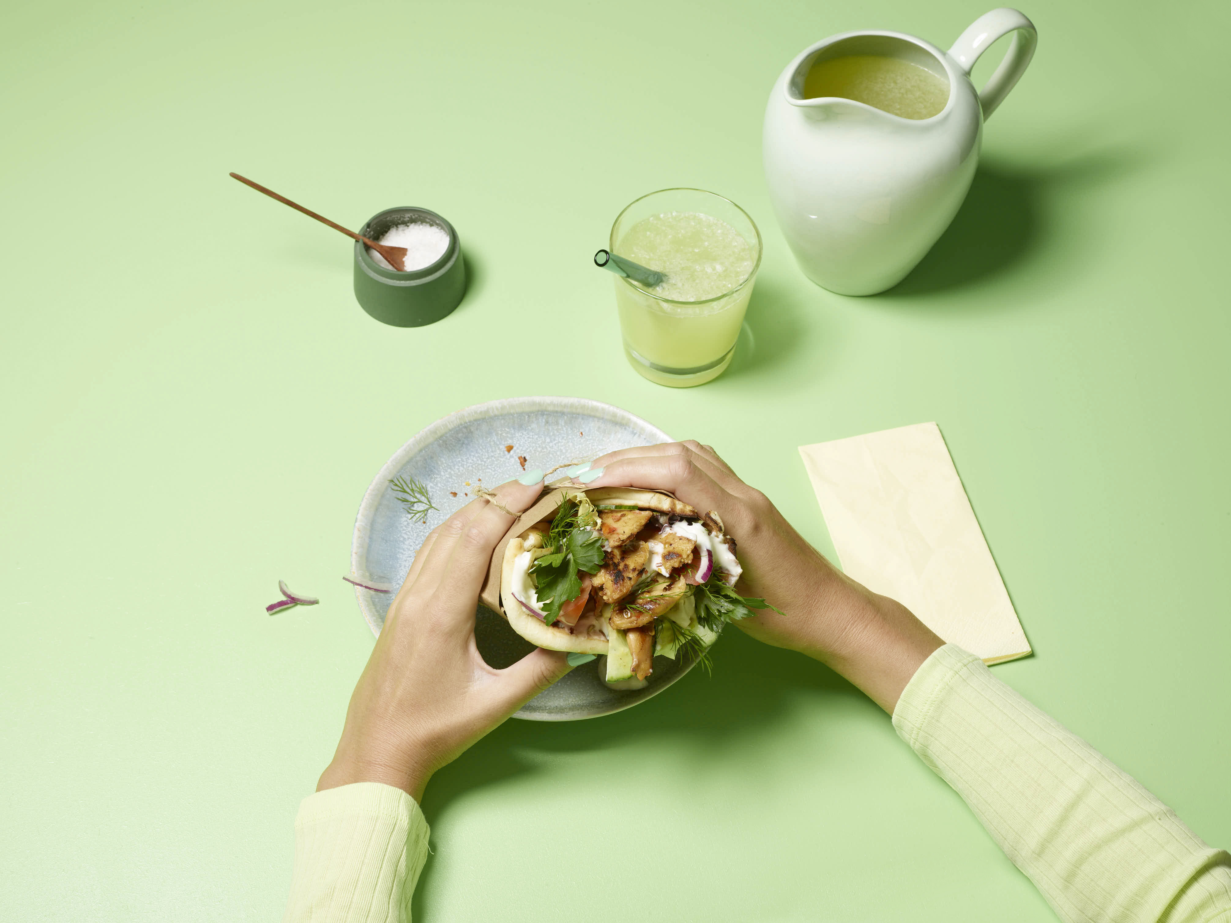 Hands holding a planted.chicken wrap on a green table