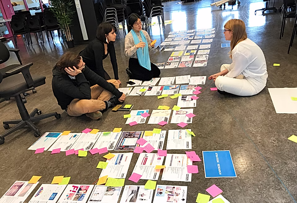 Four people reviewing research printouts laid out on the floor