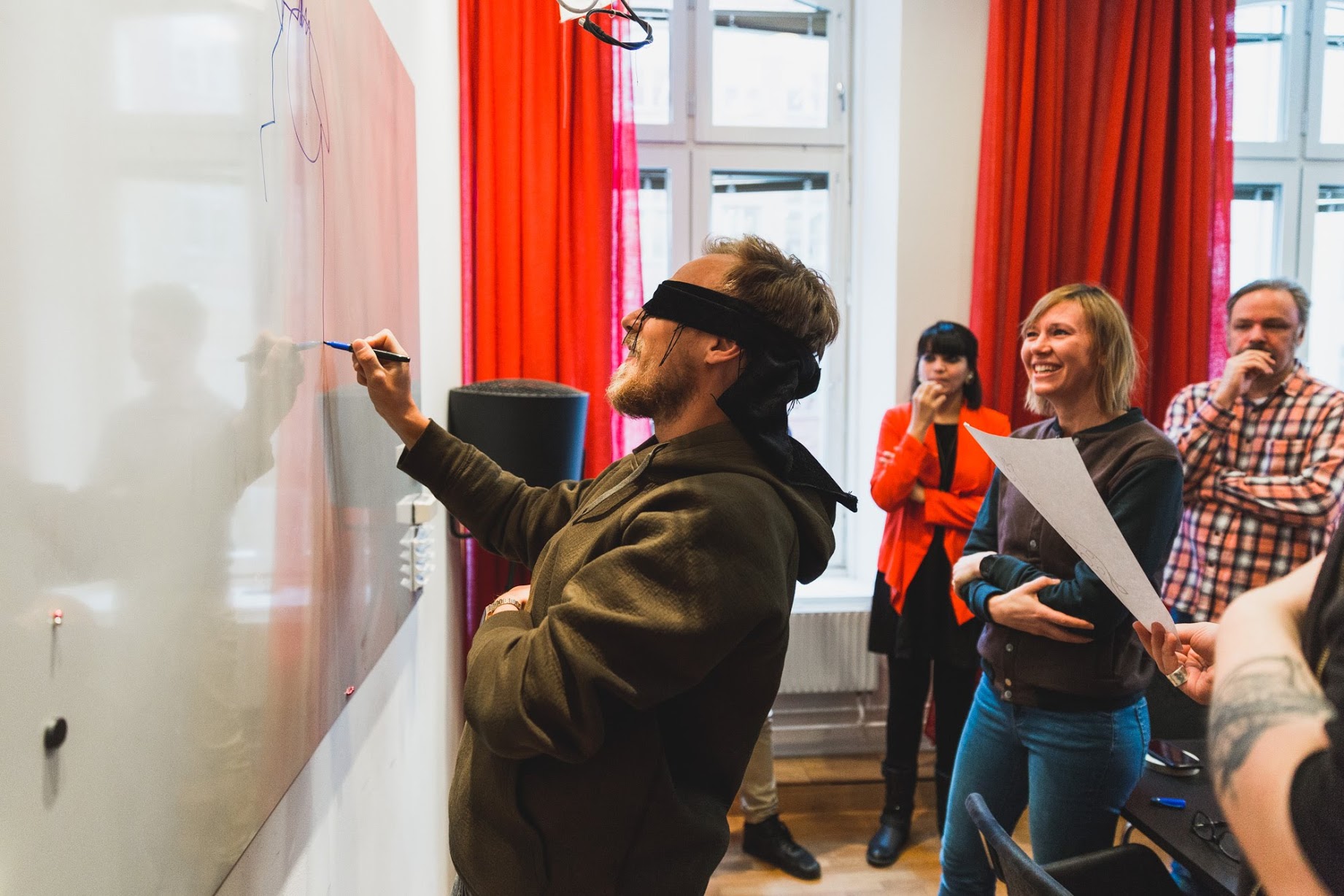 A blindfolded participant drawing on a whiteboard while the team watches